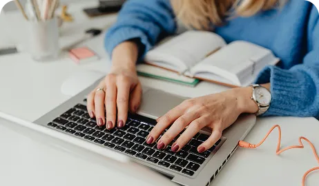 Kobieta pracuje na laptopie, siedząc przy biurku.